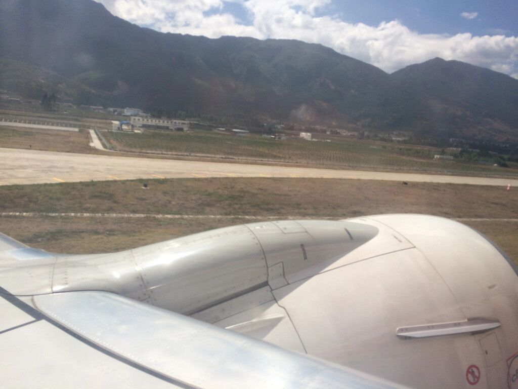 a plane wing and a runway with mountains in the background
