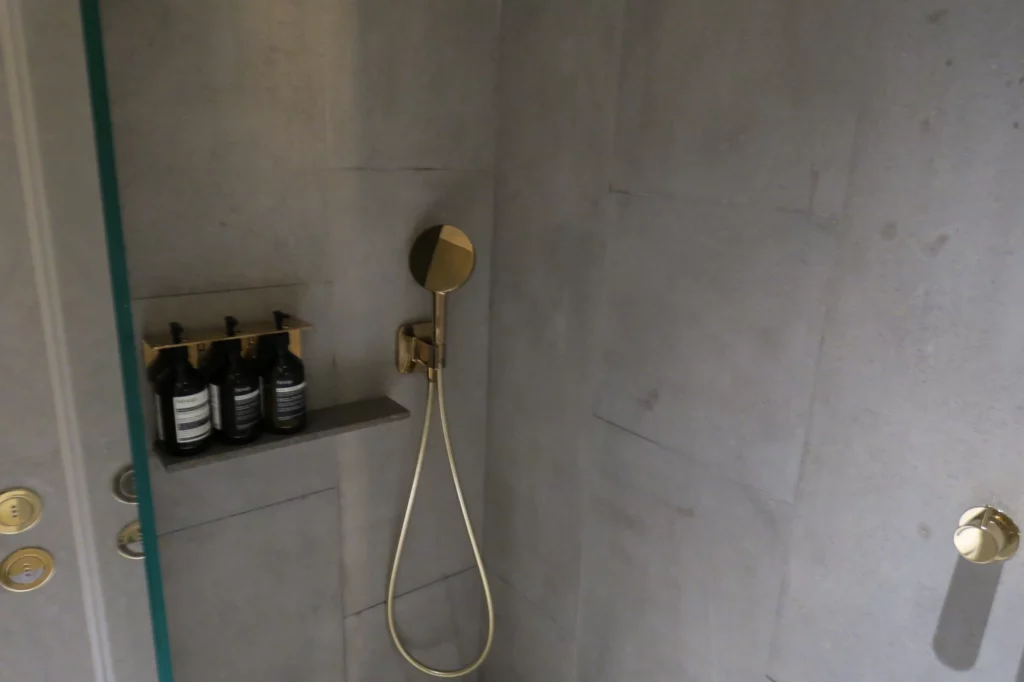 a shower with a hose and bottles on a shelf