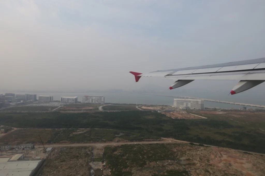 an airplane wing and land with buildings in the background