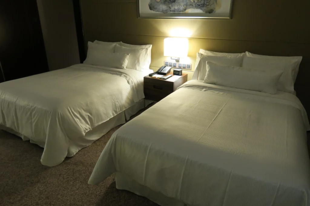 two beds with white sheets and a lamp on the side of them