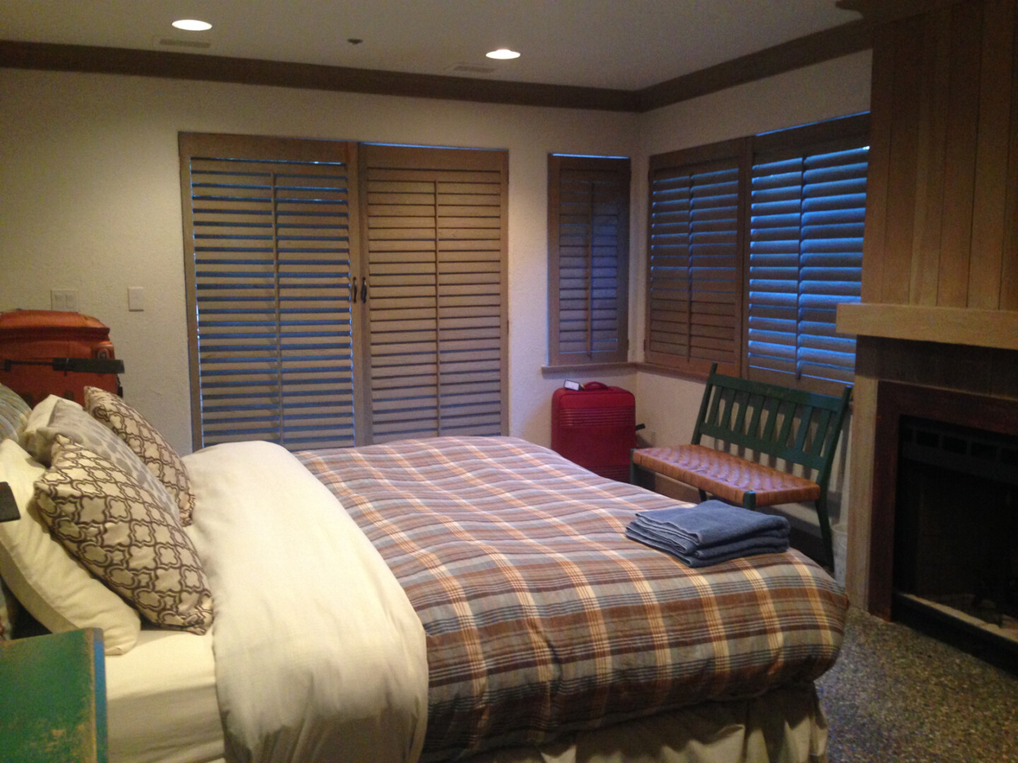 a bed with a blanket and a bench in a room with shutters