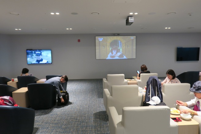 people sitting in a room with a large screen on the wall