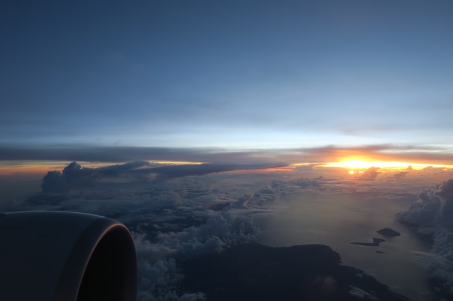 an airplane wing with the sun setting over the clouds