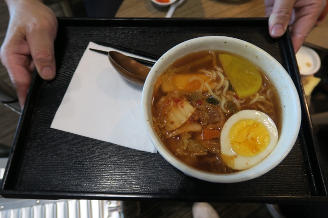a bowl of soup with egg and noodles on a tray
