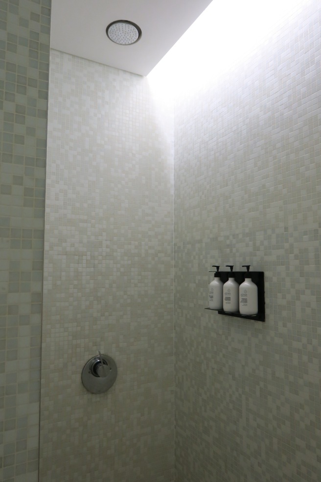 a shower with white tile walls and white bottles of shampoo