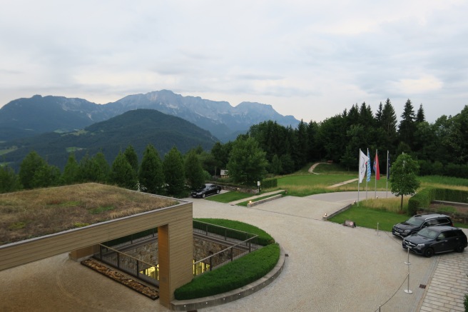 a building with a grass roof and flags in front of mountains