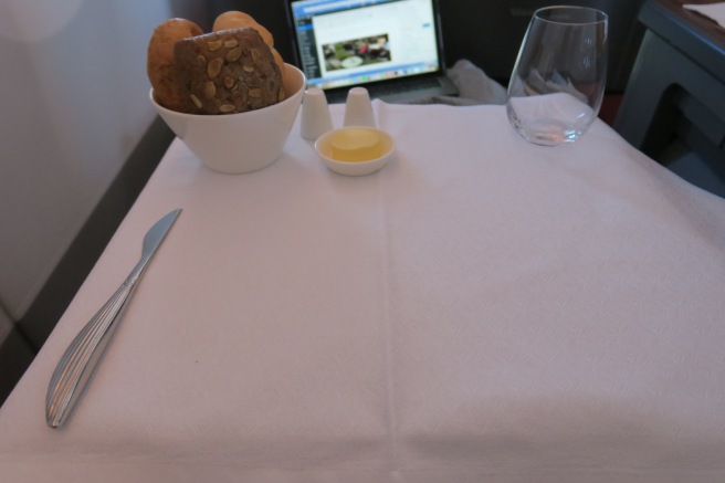 a table with a white tablecloth and a white tablecloth with a laptop and a bowl of bread and a glass of oil