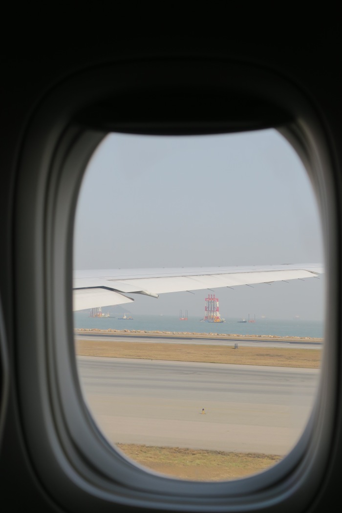 an airplane wing with a body of water and a ship in the background