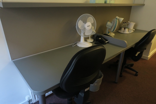 a desk with a fan and a chair