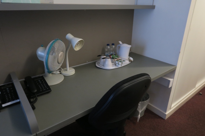a desk with a fan and a table lamp
