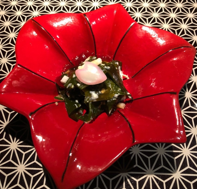 a red plate with a flower shaped bowl with a seaweed and onion