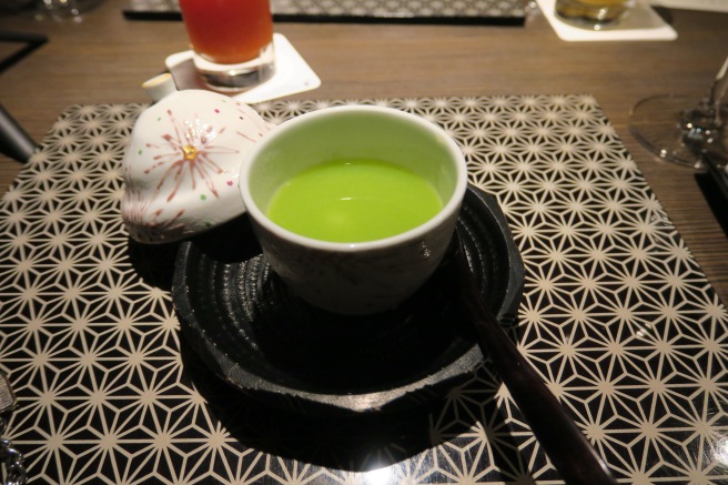a cup of green liquid on a black plate