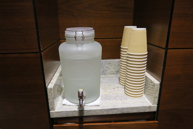 a glass container with a tap and a group of paper cups
