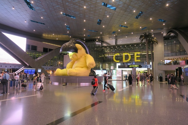 a large yellow teddy bear statue in a large airport