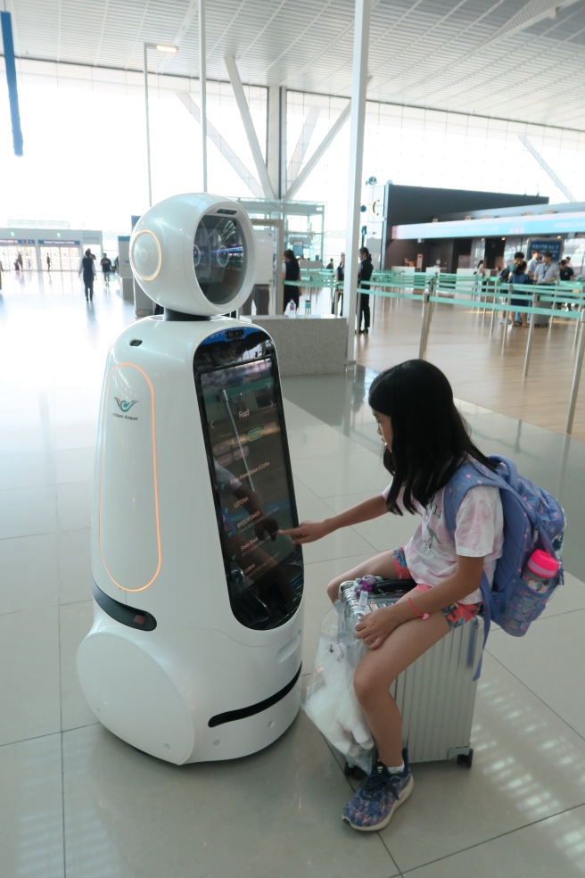 a girl sitting on a suitcase next to a robot