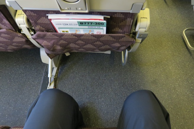 a person's legs and a seat with a magazine in the back