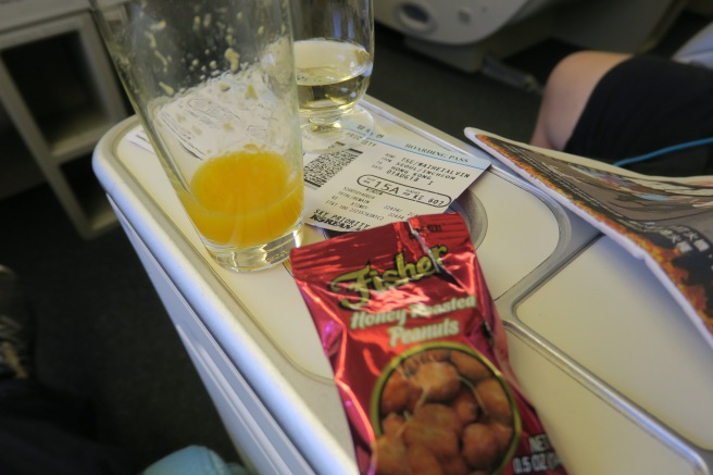 a glass of orange juice and a package of food on a plane