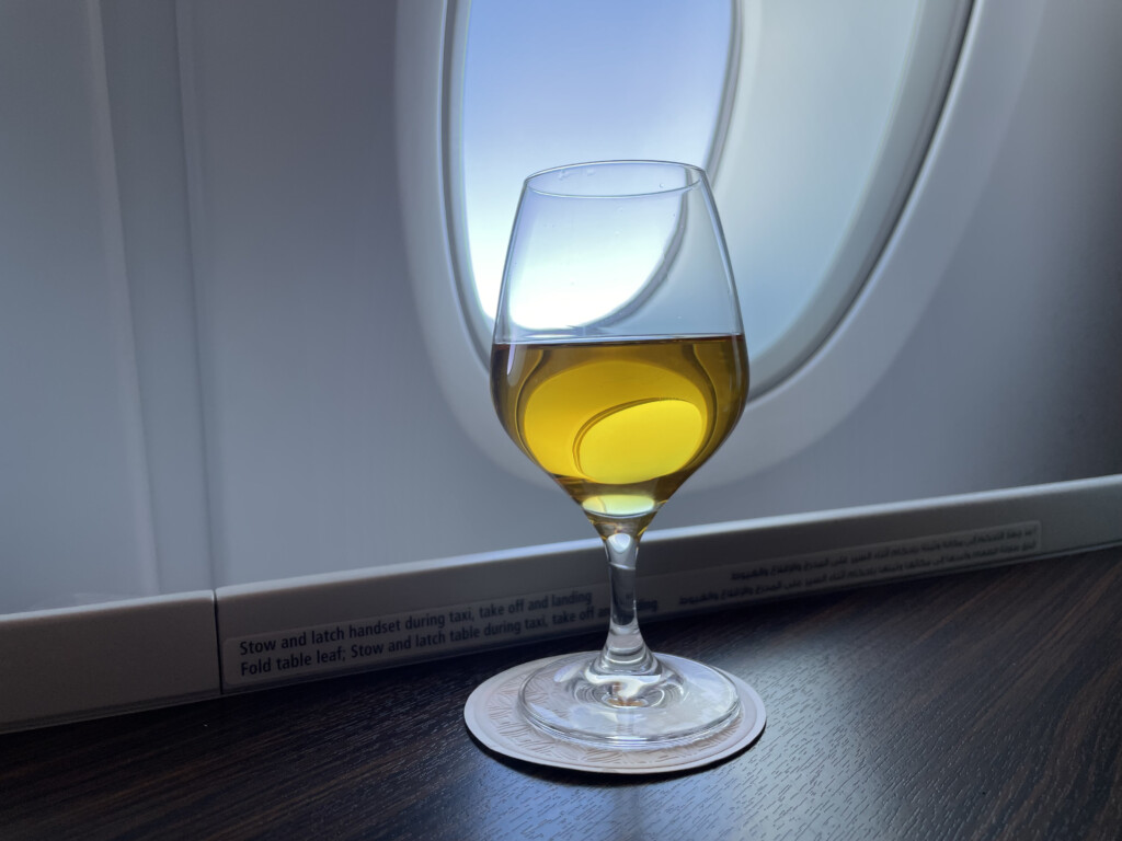 a glass of wine with yellow liquid in front of an airplane window