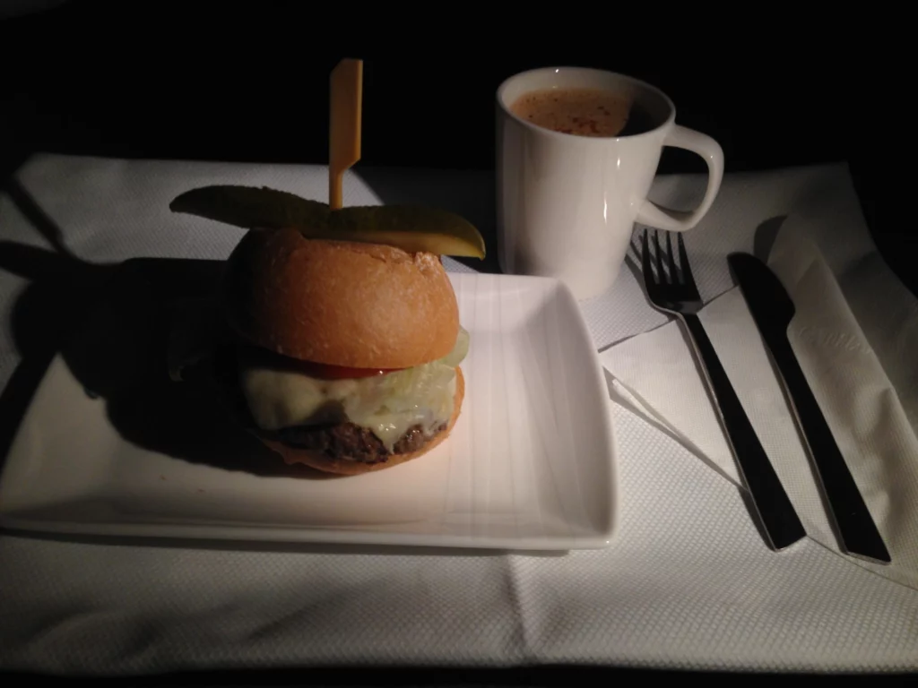 a burger on a plate next to a cup of coffee