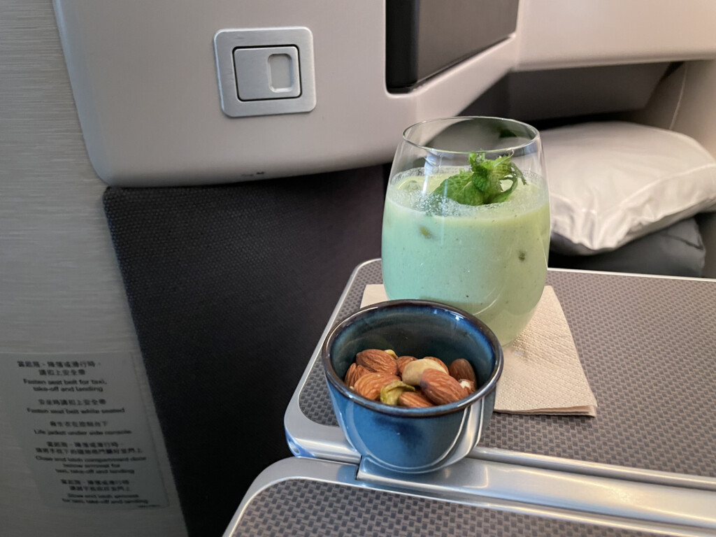 a glass of green liquid and a bowl of nuts on a table